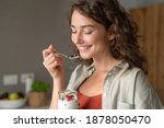 Small photo of Smiling young woman having healthy breakfast at home with fruit and yogurt. Happy natural girl holding teaspoon with yogurt and blueberries. Beautiful woman eating fresh yoghurt with berries at home.