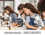 Small photo of Group of college students performing experiment using microscope in science lab. University focused student looking through microscope in biology class. High school girl examine samples during lecture