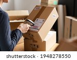 Small photo of Hands scanning barcode on delivery parcel. Worker scan barcode of cardboard packages before delivery at storage. Woman working in factory warehouse scanning labels on the boxes with barcode scanner.
