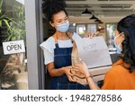 Small photo of Restaurant owner working only with take away orders during corona virus outbreak. Young black woman wearing face mask giving takeout meal to customer outside her cafeteria. Customer pick up take-away.