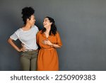 Small photo of Happy smiling multiethnic women embracing each other against grey wall with copy space. Happy laughing girls standing on grey background and looking at each other. Carefree girls having fun.