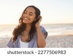 Smiling latin hispanic woman relaxing on beach with closed eyes at sunset. Beautiful mixed race woman enjoying wind fluttering hair. Charming young woman breathing fresh air at summer beach.