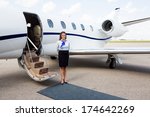 Full length portrait of airhostess standing by private jet at airport terminal