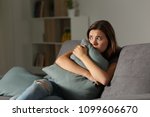 Scared teen at home embracing pillow sitting on a couch in the living room at home