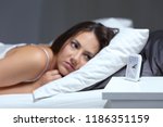 Small photo of Insomniac woman bored looking at alarm clock in the bed in the night