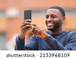 Happy man with black skin taking selfie or photo with smart phone standing in the street