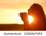 Back light silhouette of a woman smelling coffee at sunset