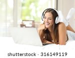 Girl with headphones listening to the music in a laptop on the bed at home