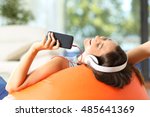Teen listening music with headphones and smart phone lying on an orange pouf in the living room at home