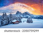 Picturesque landscape with small wooden log cabin on meadow Alpe di Siusi on sunset time. Seiser Alm, Dolomites, Italy. Snowy hills with orange larch and Sassolungo and Langkofel mountains group