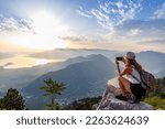 A happy girl with a backpack photographs the seascapes of Montenegro from the top of the mountain