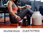 Small photo of A sportswoman is taking a break in a gym and reaching for supplements and pre workout pills. Selective focus on hand with bottle.