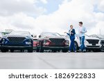 Positive female car dealership saleswoman walking along rows of new cars with customer