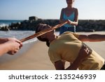 Small photo of Young man bending backwards and passing under ribbon when ing limbo game with friends on beach