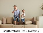 Two little brothers standing on sofa at home and singing into microphones together