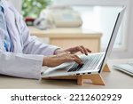 Close-up of female doctor sitting at her workplace at office and typing on laptop doing online work
