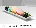 Small photo of Filled macaroons each of different color (blue, yellow, pink) prearranged on a rectangle plate decorated with blueberries, raspberries and mint leaves on a black and white background