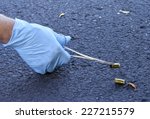 Crime scene investigator is gathering evidence by picking up shell casing using rubber gloves and a forcepts.