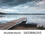 Morning landscape. The shore of the lake with a wooden pier and tied the boat at dawn. The water reflects the sky. A light fog is spreading over the water. As a concept of outdoor recreation.