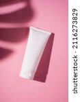 Small photo of Plastic white tube for cream or lotion. Skin care or sunscreen cosmetic in top view on pink background with palm leaves shadow. Beauty concept for face care