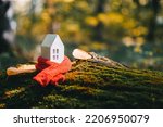 Small photo of Miniature house in a red scarf on an autumn background with moss and yellow leaves. The concept of passive house heating. Thermal insulation of a building or dwelling. Energy crisis.