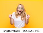 Small photo of young pretty blonde woman feeling shocked, excited and happy, laughing and celebrating success, saying wow! against flat color wall