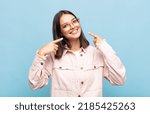 Small photo of young pretty woman smiling confidently pointing to own broad smile, positive, relaxed, satisfied attitude