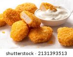 Small photo of Fried gluten free cornflake crumb chicken nuggets next to a bowl of white sauce on white baking paper. Dipped nugget.