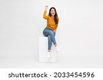 Attractive beautiful Asian woman sitting on white box and hands up raised arms from happiness, Excited female and winner success concept