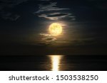 Super full moon cloudy in dark sky on the ocean horizon at midnight, Moonlight yellow gold reflects the wave water surface, Beautiful fantasy nature landscape view the sea at night scene background