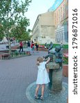 Small photo of Lodz / Poland. 03 August 2019: Little girl washing hands in city statue fountain. Statue of fountain in shape of girl and fish in city of Lodz. Little girl in white dress is naught with water in city