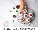 Woman hand picking small Christmas bundt cakes with sugar glaze and  currants on a rustic wood slice. Top view