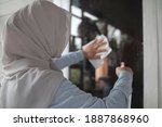Small photo of Muslim woman cleaning window glass with wag and spray, outdoor home window