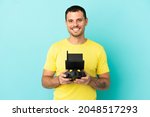 Brazilian man holding a drone remote control over isolated blue background posing with arms at hip and smiling