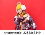 Small photo of Young beautiful woman wearing winter muffs isolated on red background suffering from pain in shoulder for having made an effort
