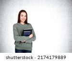 Small photo of Attractive businesswoman wearing casual wear is standing holding notebook near empty white wall in background. Concept of working process, taking notes for daily schedule, scorekeeper and secretary