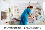 Small photo of Female nurse helping an old lady to go to bed and covers her with a blanket in a nursing retirement home with big windows