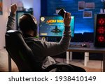 Small photo of Winner gamer sitting on gaming chair at desk and playing space shooter video games with controller. Man streaming online videogames for esport tournament in room with neon lights