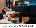 Small photo of Person sleeping on sofa after drinking beer and eating home delivery pizza in front of television in living room. Tired woman falling asleep couch after large fast food takeout meal.