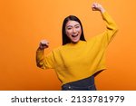 Motivated triumphant girl celebrating victory and feeling optimistic and independent. Positive optimistic woman raising arms while feeling strong and confident on orange background.