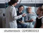Small photo of Elderly people care nurse reviewing files of senior male patient bedridden in geriatric hospital. Female general practitioner listening to older hospitalized man symptoms.