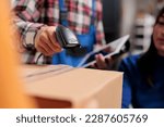 Small photo of Retail storehouse employees doing inventory management while scanning packages. Postal service warehouse manager holding barcode scanner and digital tablet in arm close up