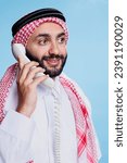 Small photo of Smiling man wearing traditional muslim red and white checkered headdress chatting on landline phone. Cheerful person in checkered arabic headdress with rope band having fun conversation on telephone
