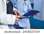 Small photo of Doctor using a digital tablet in medical office while wearing a lab coat. Nurse waits with clipboard in background with selective focus on masculine hands grasping a smart gadget.