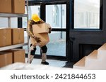 Small photo of Delivery service african american loader carrying heave cardboard boxes and standing in warehouse office doors. Shipping company man employee carrying parcels in storage room