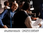 Small photo of Couturiers manufacturing bespoken clothing, working together to finalize client sartorial comission. Master tailor and diverse apprentice team of suitmakers checking fashion design sketches in atelier
