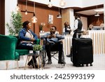 Traveling with wheelchair user. Tired unhappy couple woman and disabled man waiting for registration at resort, sitting with luggage in hotel lobby, customer service for guests with disabilities