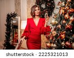 New Year Party, holidays, christmas and celebration concept. Beautiful girl in red dress with glass of sparkling wine near Christmas tree in decorated living room