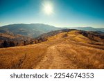 Mountain landscape on a sunny day in autumn. View of the mountain slopes and dirt road. Beautiful nature landscape. Carpathian mountains. Ukraine