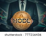 businessman holding big shiny bitcoin in hands in front of stock market data chart background and hodl word on bitcoin